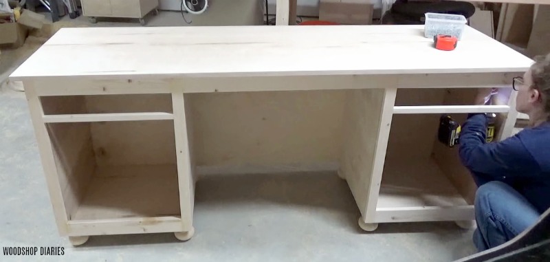 Shara Woodshop Diaries securing top of desk using screws from inside of cabinets in workshop