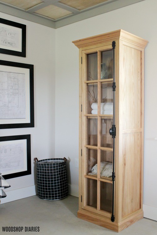 DIY Red oak linen cabinet with crown molding, baseboard trim, and a glass door