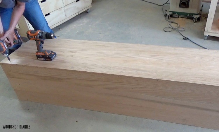 Shara Woodshop Diaries installing back panel onto DIY linen cabinet with glass door on workshop floor