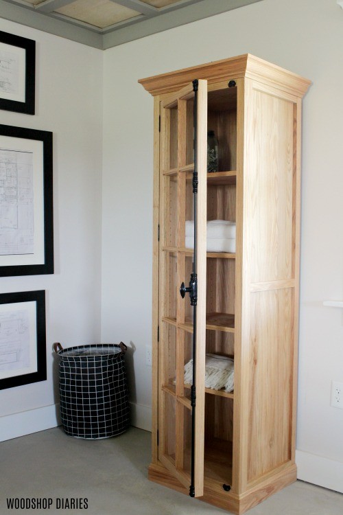 Finished DIY linen cabinet with glass door and cremone bolt--door half open to show inside shelves