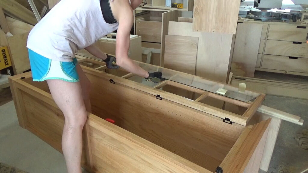 Shara Woodshop Diaries installing glass panel into door frame on linen cabinet