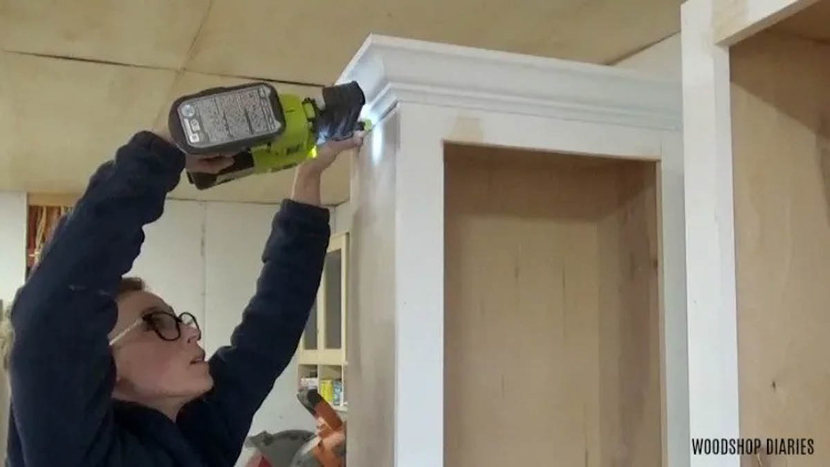 Shara Woodshop Diaries nailing crown molding onto top of side cabinets of entertainment center