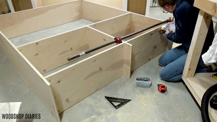Shara Woodshop Diaries installing the bottom panels of large cabinet on workshop floor