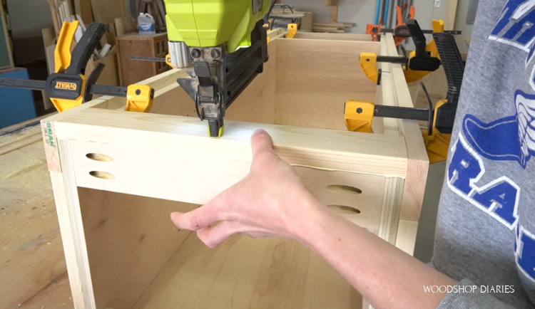 Using brad nailer to attach front face frame piece to linen cabinet