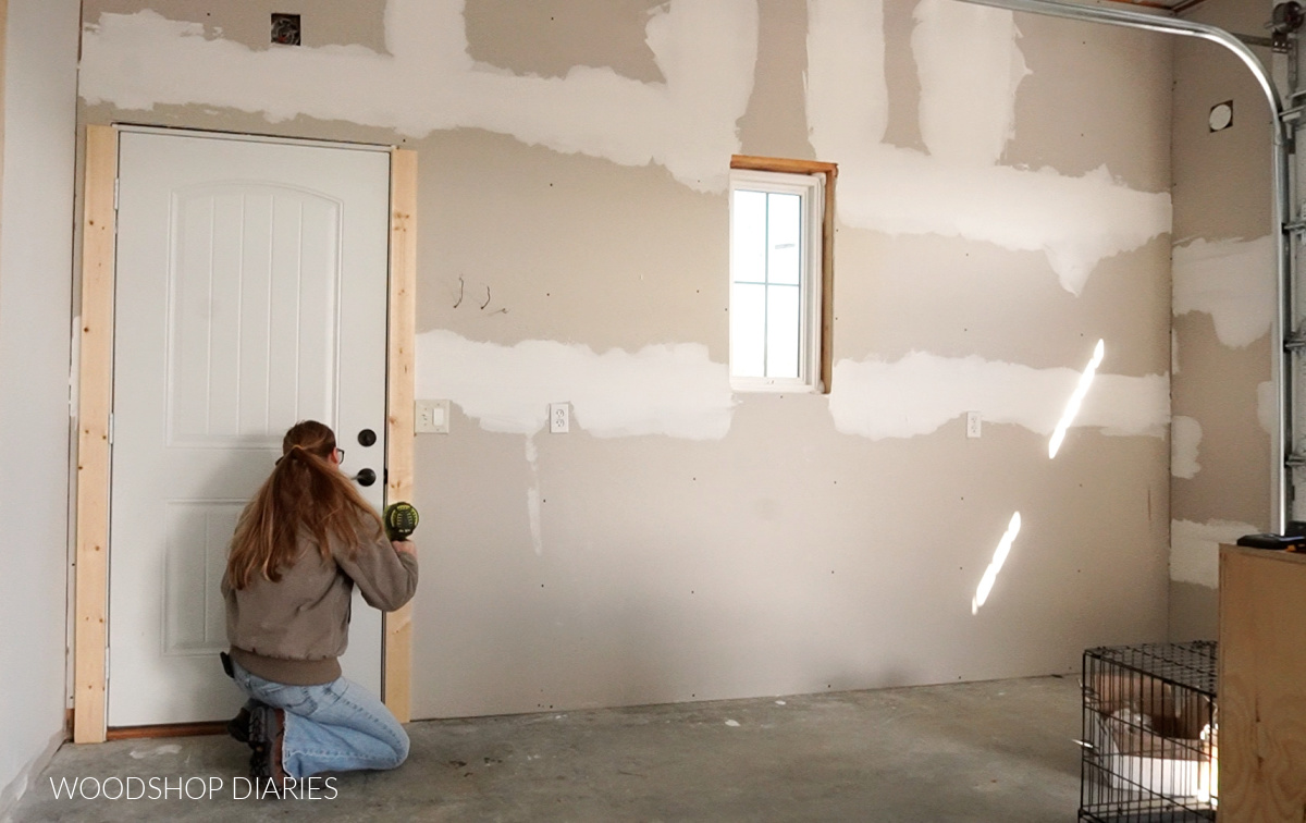 Shara nailing door trim around door of Unfinished drywall wall in workshop