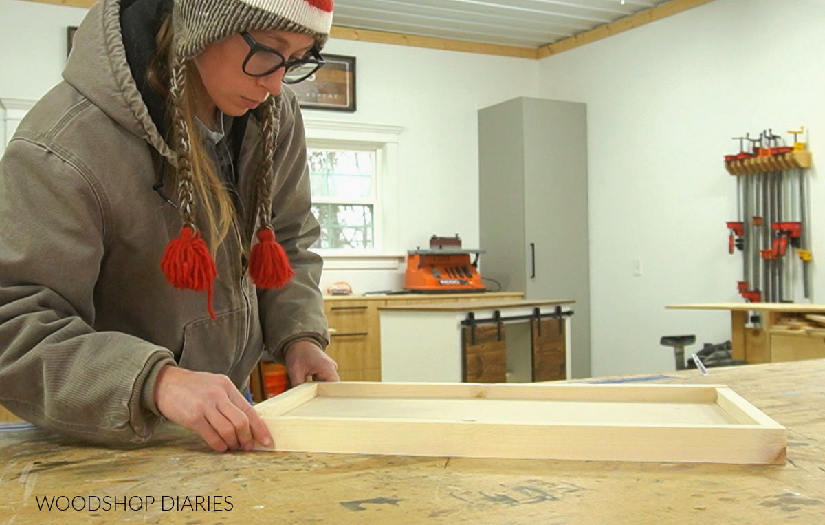 Shara Woodshop Diaries dry fitting 1x2 frame around shelf panel on workbench