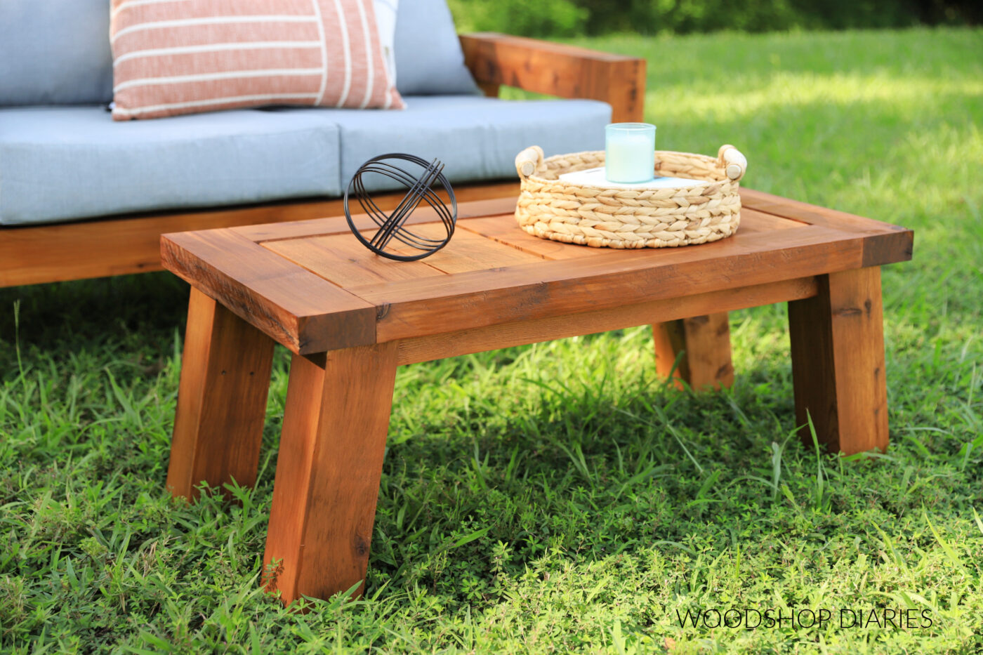 Beautiful wooden outdoor coffee table with wicker tray in front of wooden loveseat in grassy area