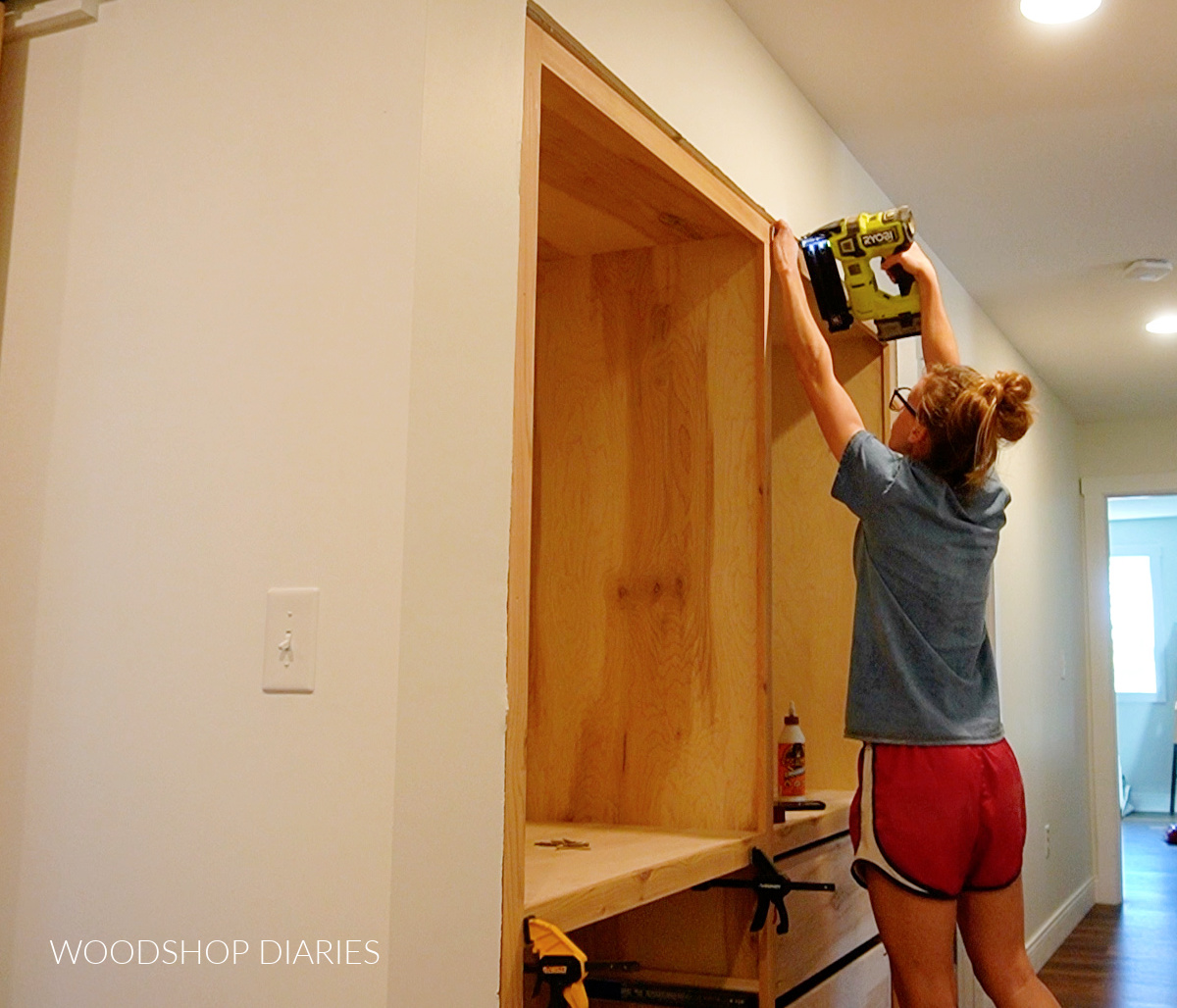 Top cabinet installed into opening and Shara Woodshop Diaries nailing face frame onto front