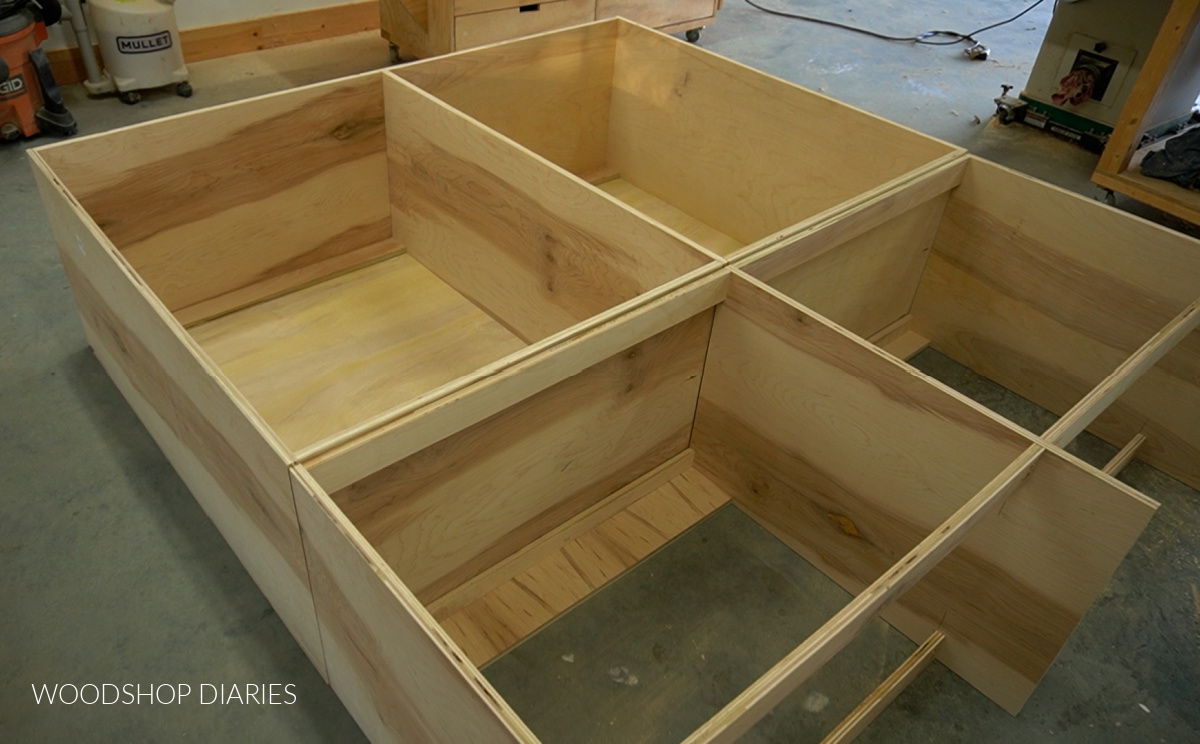 Two large cabinets assembled on workshop floor--top cabinets open for shelves bottom cabinet for drawers