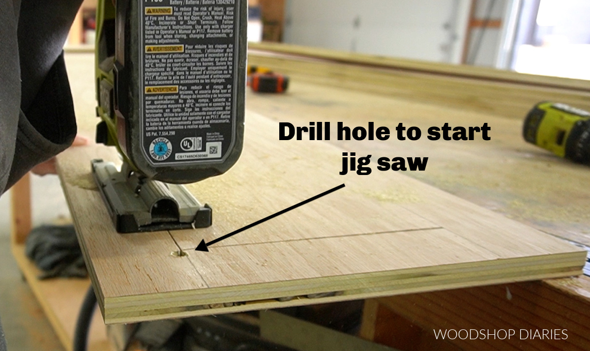 Jig saw cutting out drawer opening in side panels--arrow pointing to the hole drilled outside the line to start the blade from