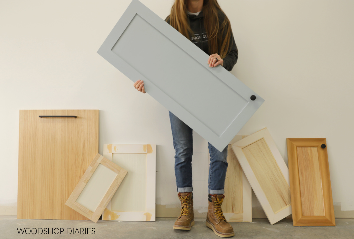Shara Woodshop Diaries holding a door with 6 more doors leaning against the wall in the background