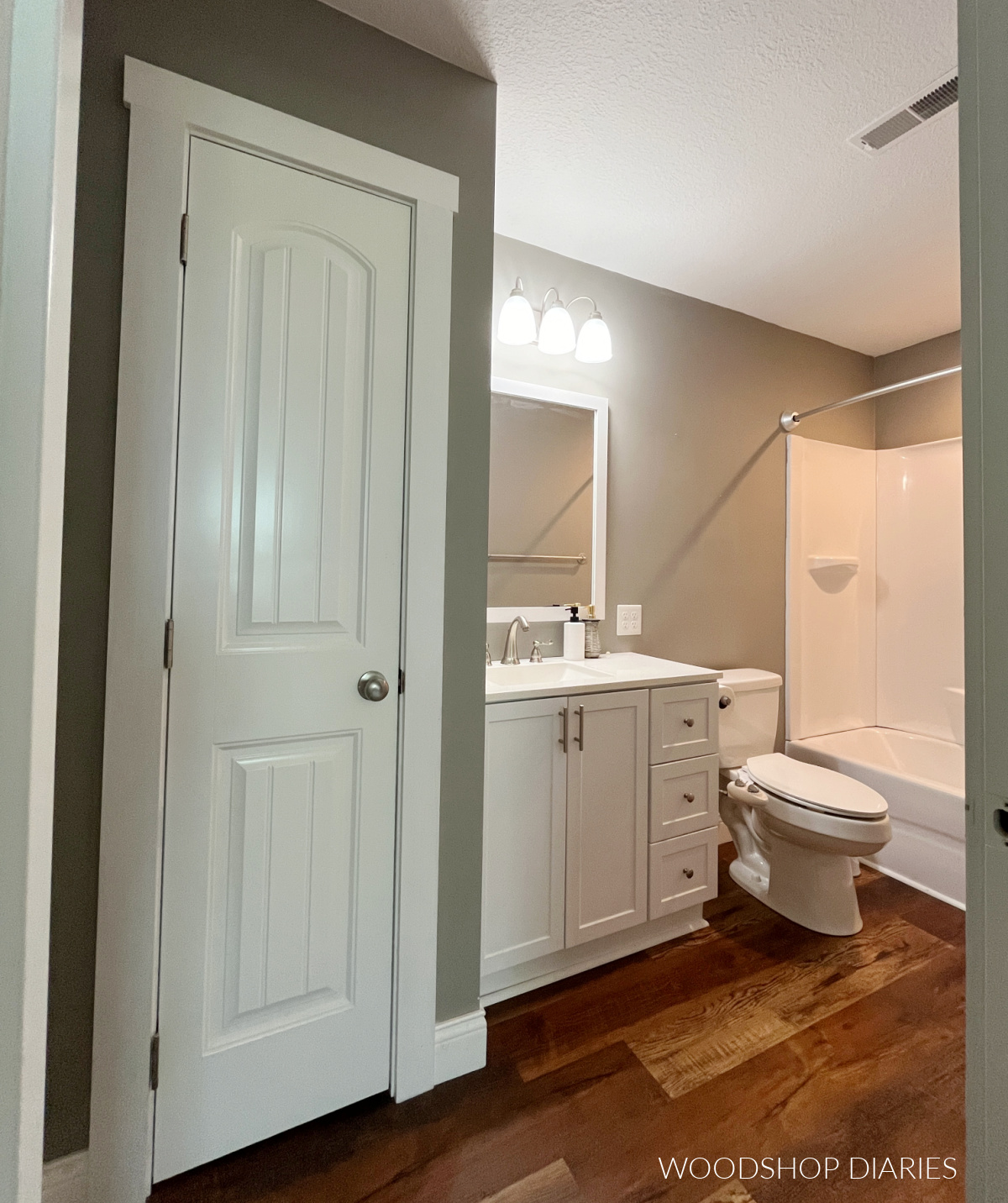 Small guest bathroom before the makeover--white vanity, grey walls, wood floor
