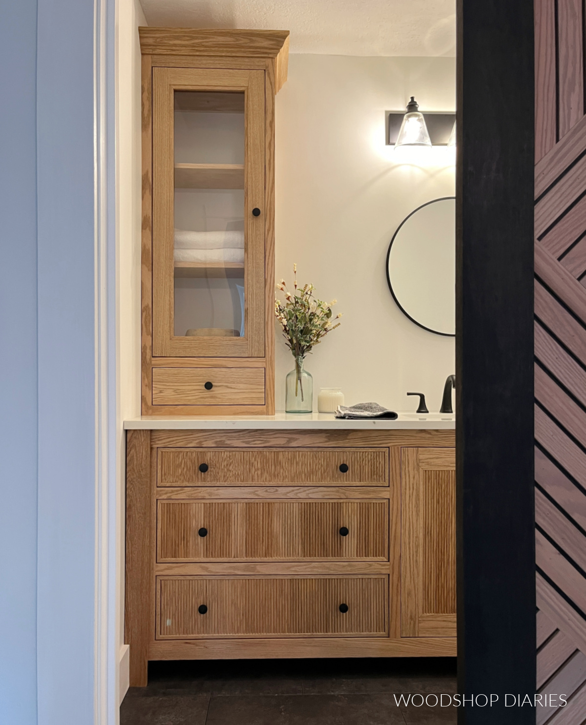 View into small updated bathroom showing view of fluted drawer front vanity and tall cabinet on countertop