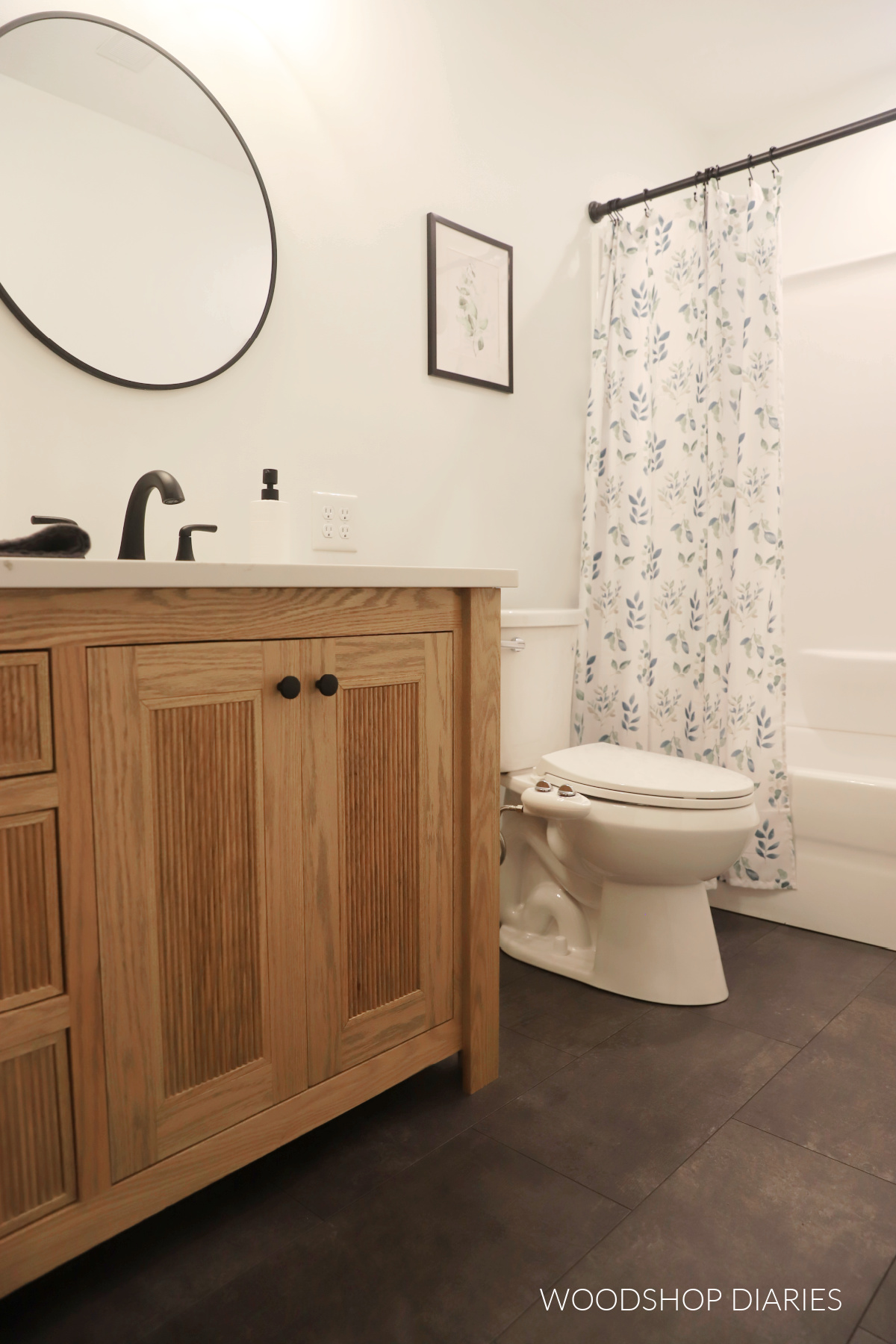 Finished modern makeover of small bathroom showing white walls, new toilet, corner of wood vanity and mirror
