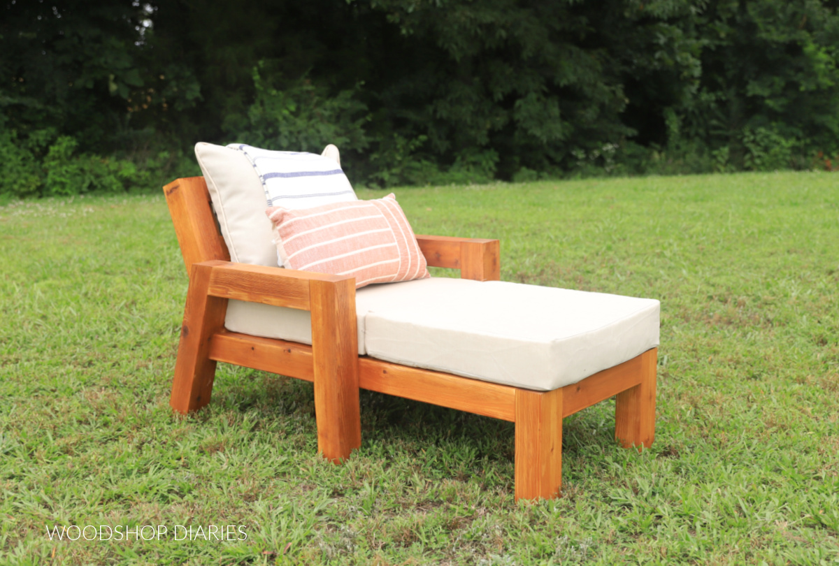 Outdoor wooden chaise lounge chair in grass with tan cushions
