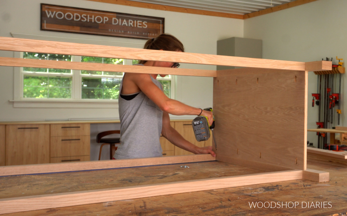 Shara Woodshop Diaries attaching side panels of 9 drawer dresser between front and back frames on workbench