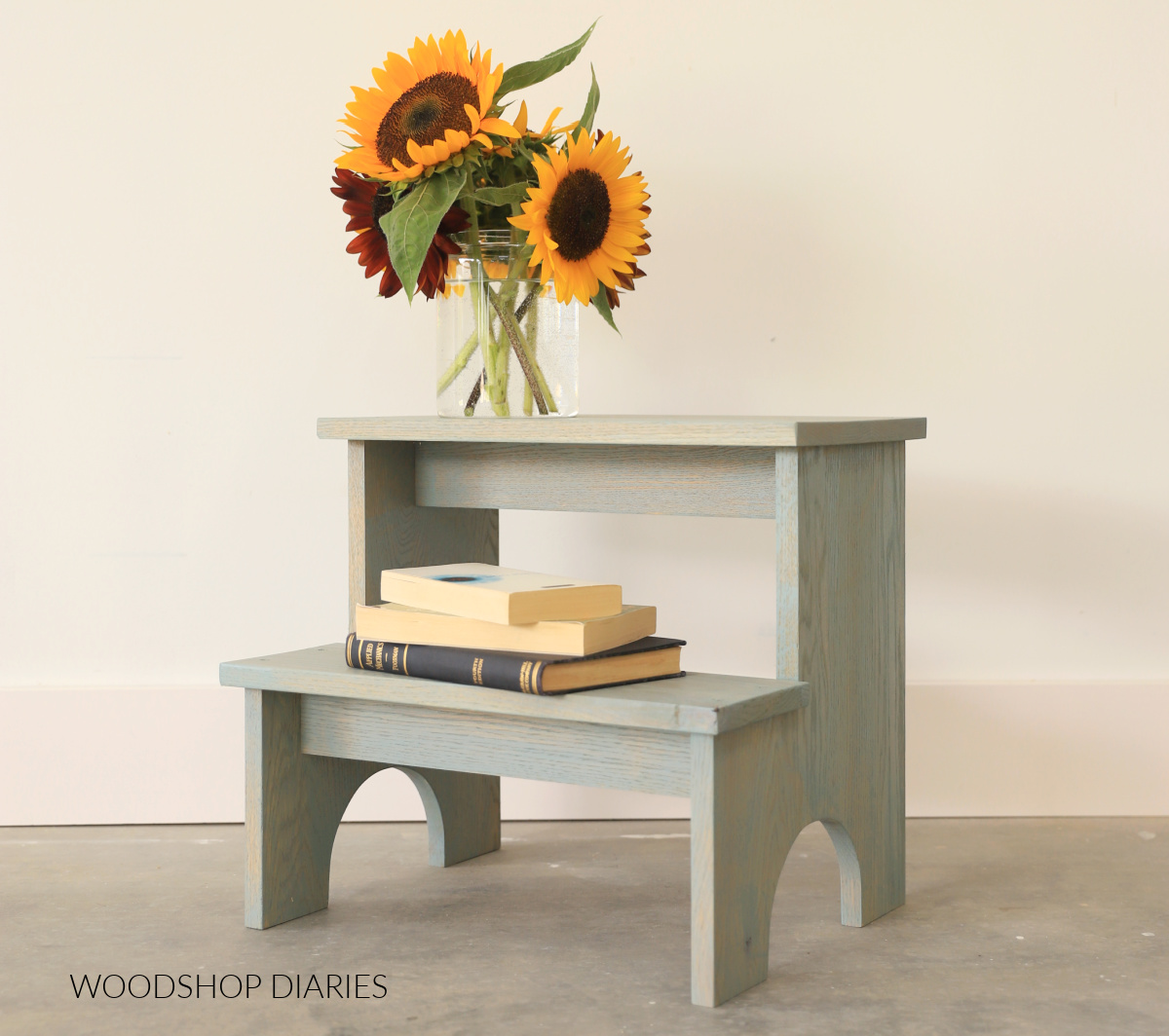 green stained side table with sunflowers and books against white wall