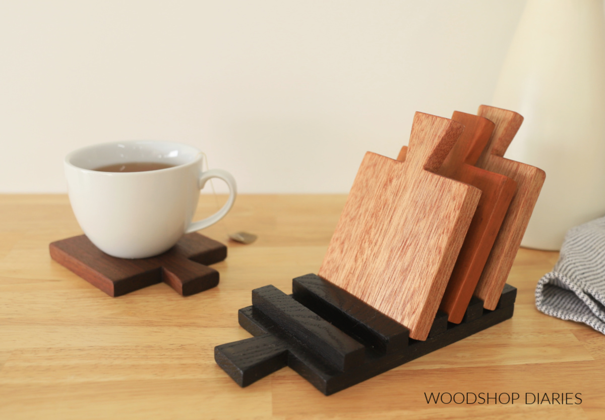 cutting board shaped wooden drink coaster set with wooden display tray in different wood types with mug of tea sitting on one