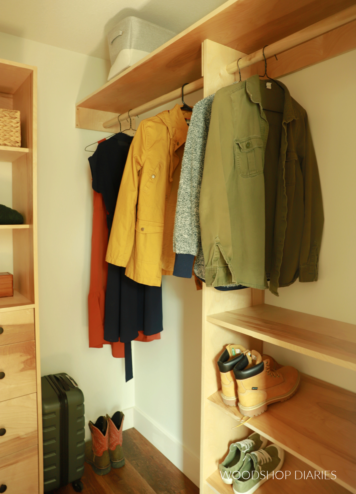 Small walk in closet with hanging rod and plywood cabinets with shirts and dresses hanging up