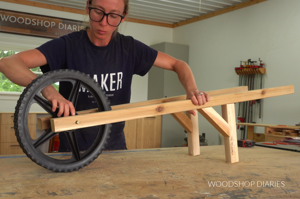 Shara Woodshop Diaries fitting wheel into wooden wheelbarrow supports