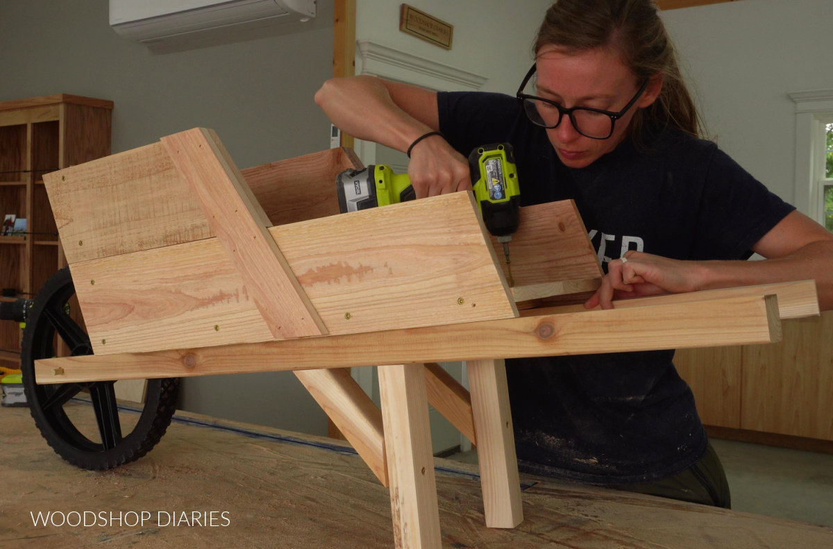 Shara Woodshop Diaries screwing wheelbarrow body to supports 