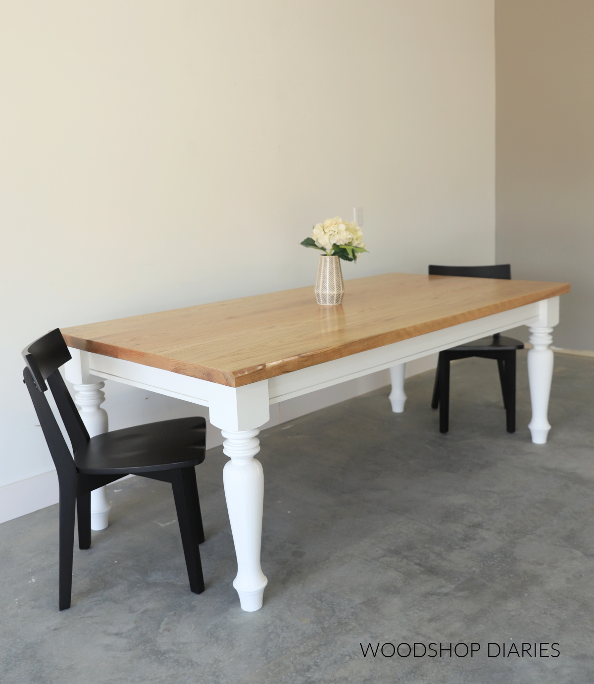 Finished DIY dining table with white painted base and wood stained table top with two black chairs at each end
