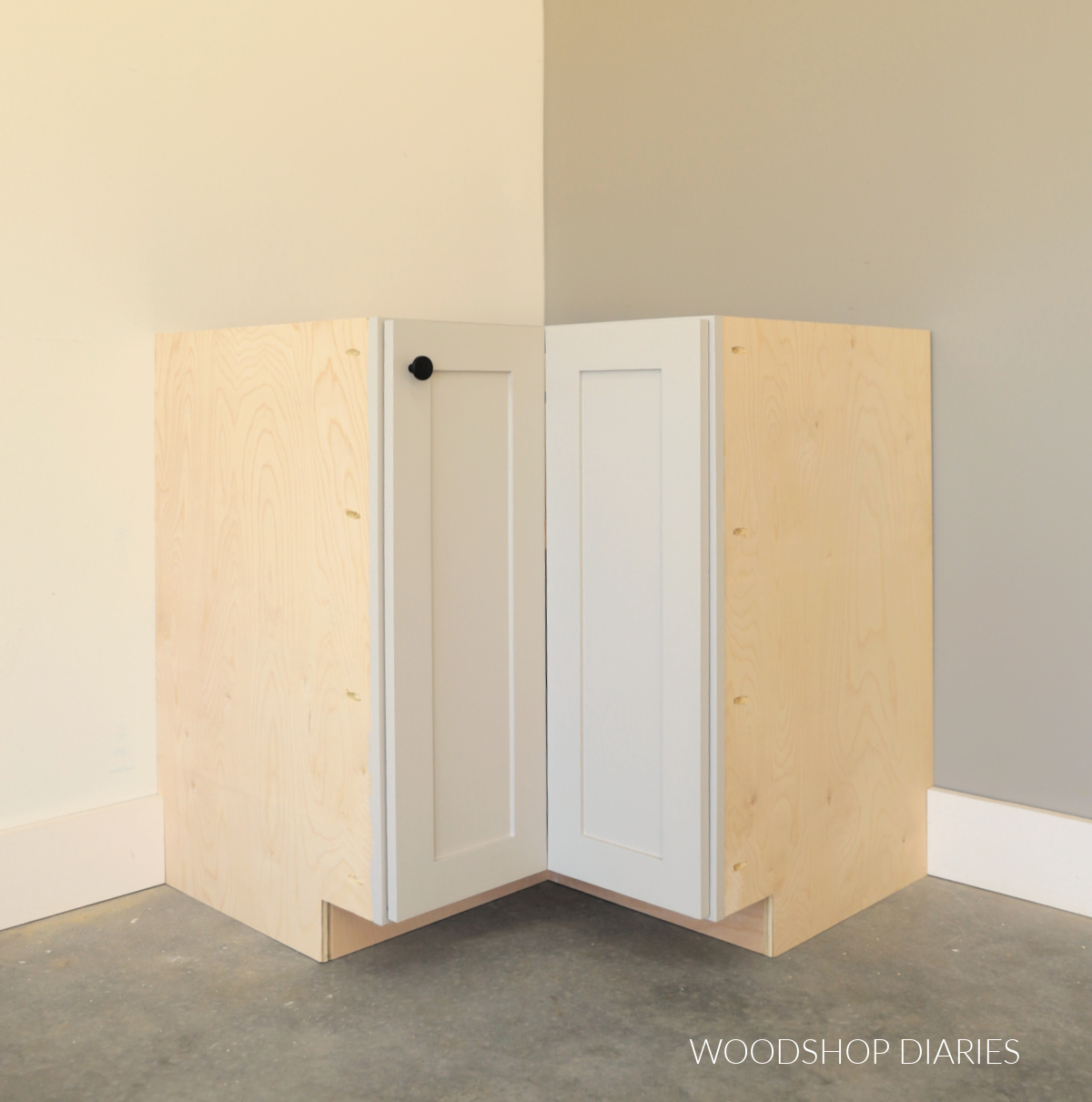 Completed DIY corner base cabinet with bi-fold doors sitting in corner of room