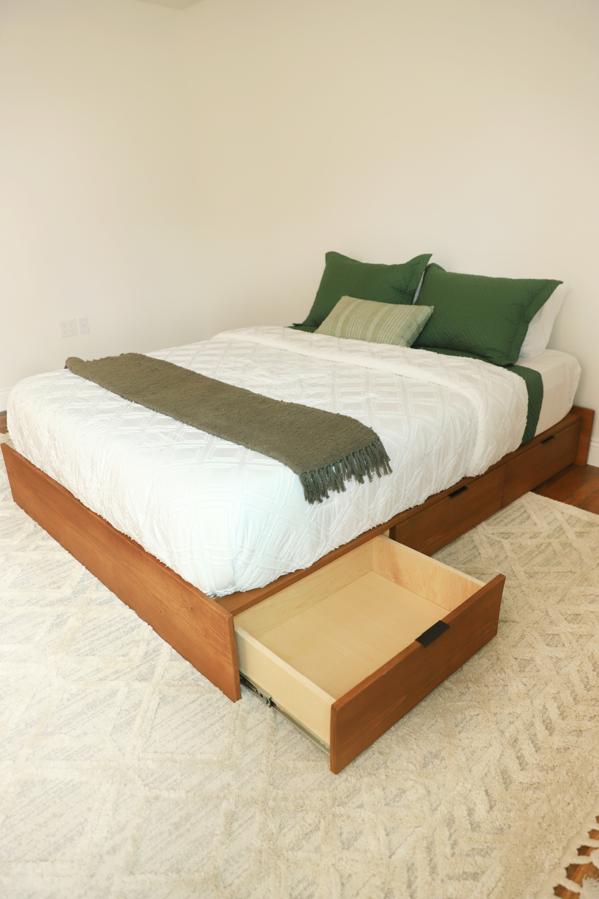 DIY wooden platform bed with storage drawers--one drawer open--with white bedding and green pillows