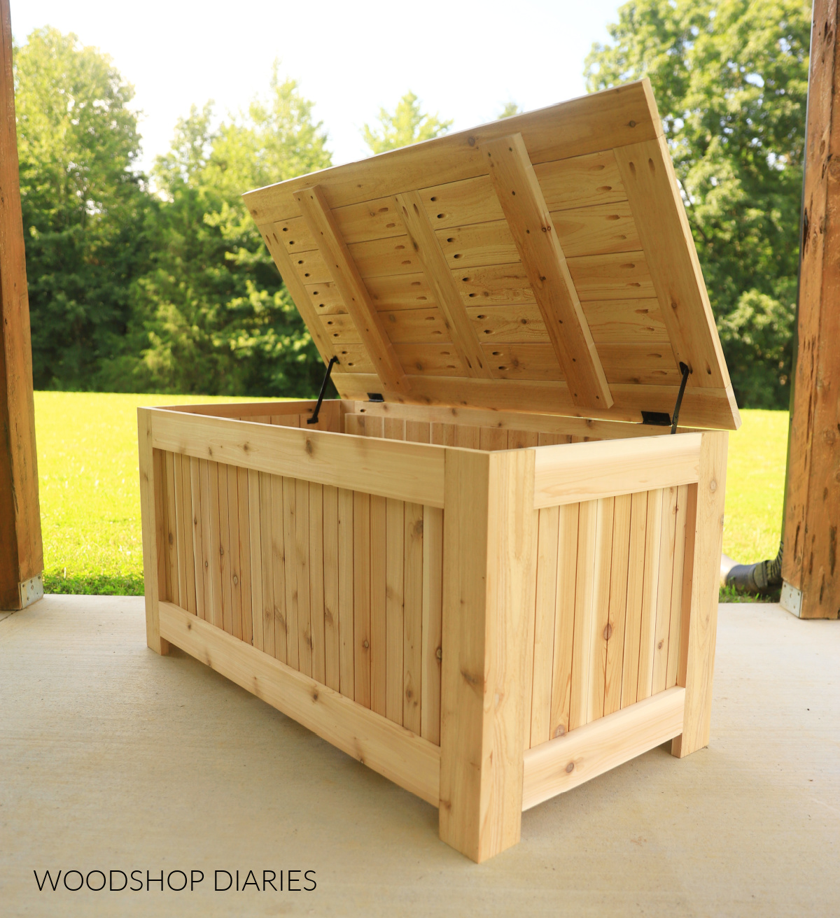DIY outdoor storage box built with cedar 1x4s with lid in open position on porch