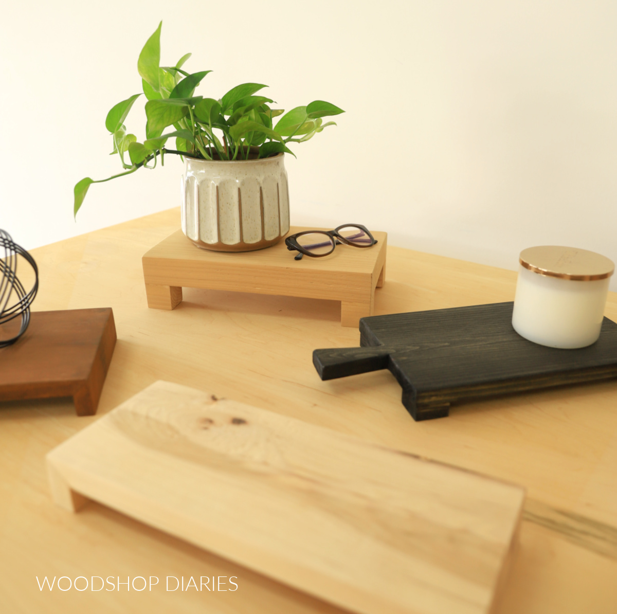 Assorted wooden risers in different shapes and sizes on workbench top with plant and glasses resting on one