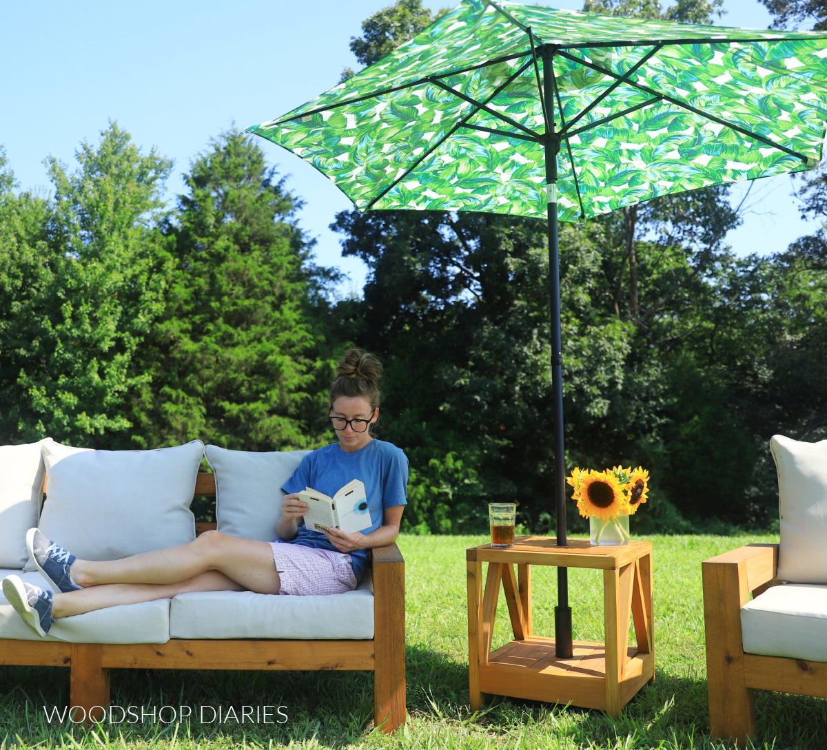 Shara Woodshop Diaries sitting on outdoor sofa next to umbrella stand side table with palm leaf umbrella providing shade