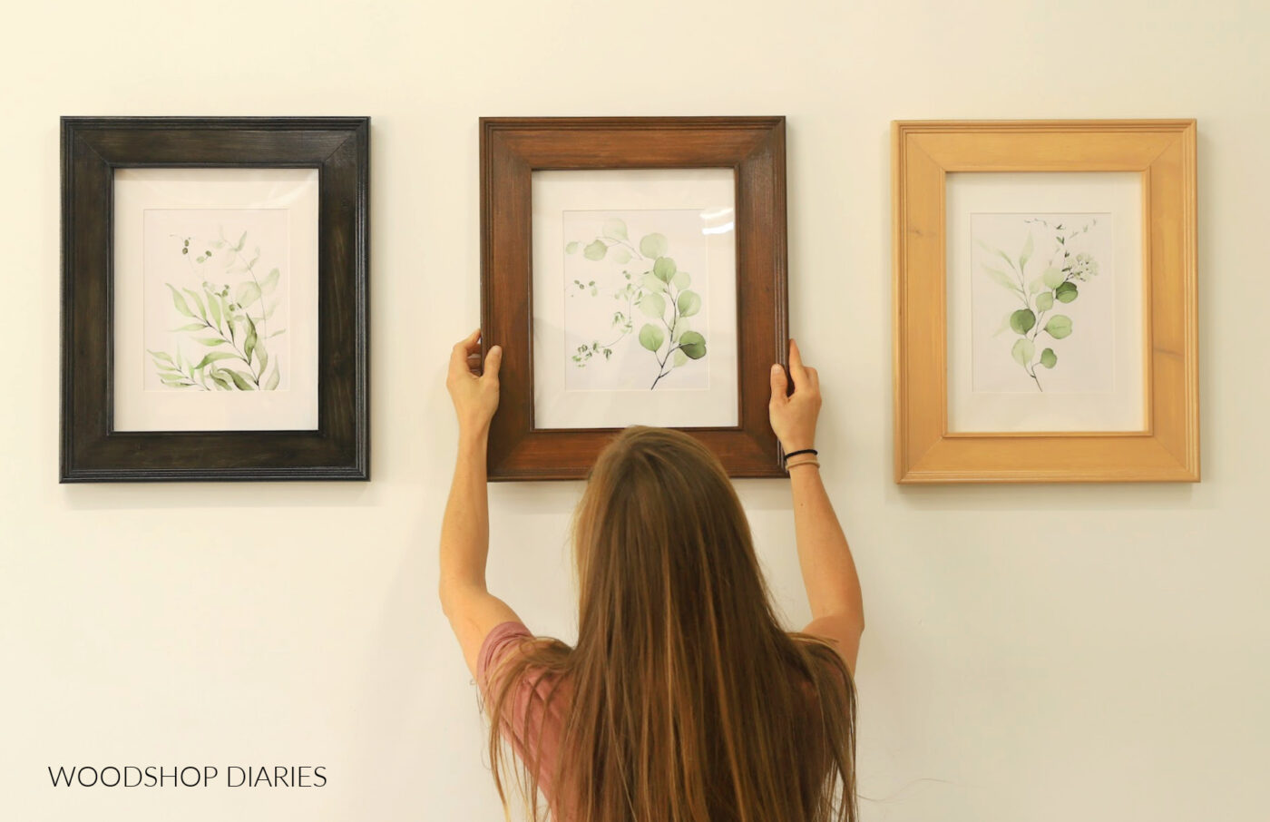 Shara Woodshop Diaries hanging one of three wooden DIY picture frames on wall 