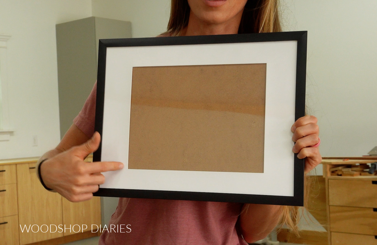 Shara Woodshop Diaries holding up cheap black picture frame in workshop