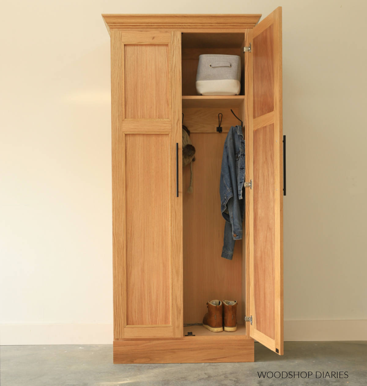 Red oak armoire cabinet with double doors for coat storage. One door open to reveal the inside with hooks and a shelf