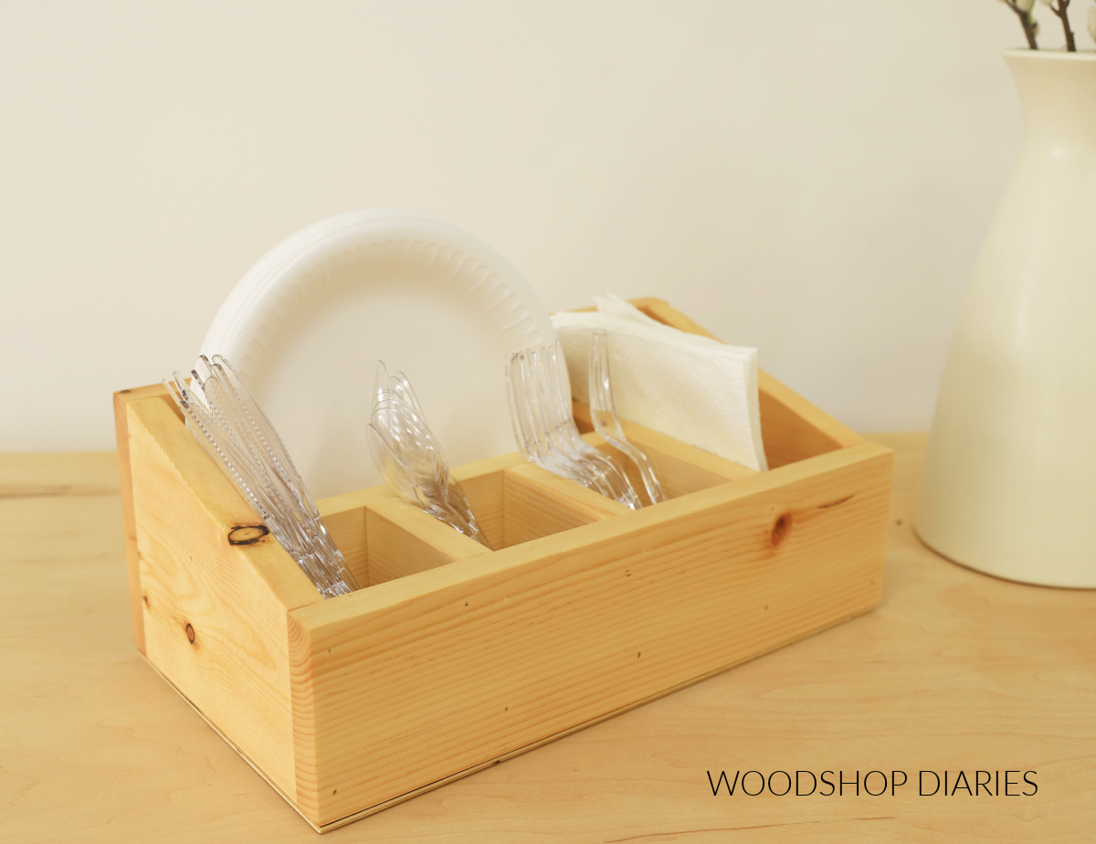 wooden utensil caddy for disposable dinnerware with paper plates, napkins, and plastic cutlery in between dividers