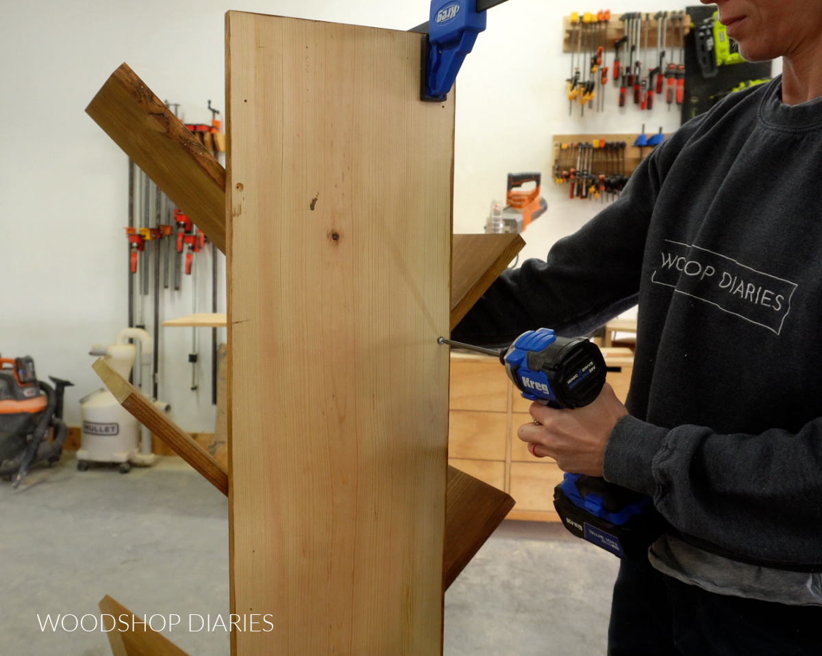 Shara Woodshop Diaries driving screws through back of bookshelf to secure each angled shelf piece