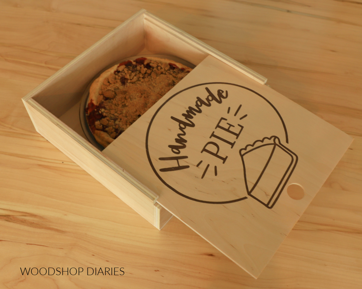 Scrap plywood pie box with sliding lid and "handmade pie" logo on top revealing a pie inside