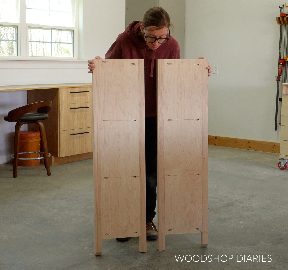 Shara Woodshop Diaries holding two DIY small bookcase side panels in workshop