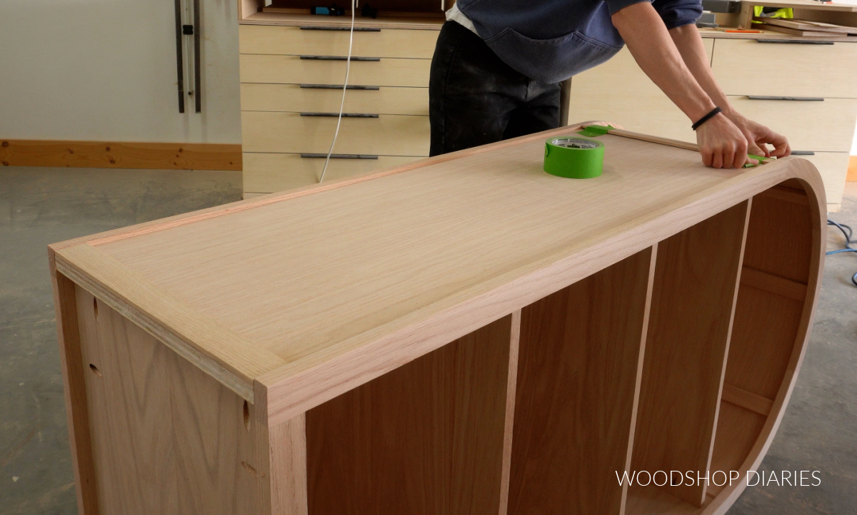 Close up of gluing and taping trim pieces onto cabinet sides