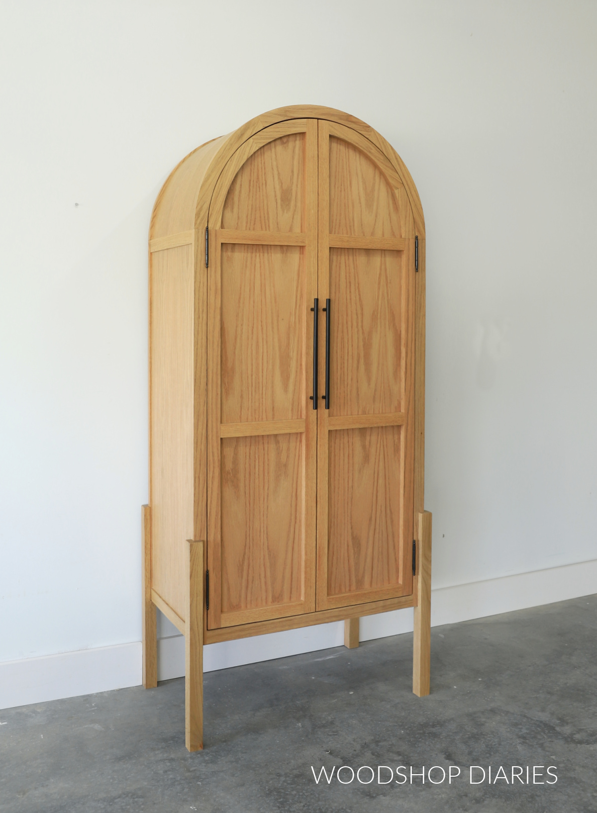 Completed DIY arched cabinet with double doors and modern legs made from red oak